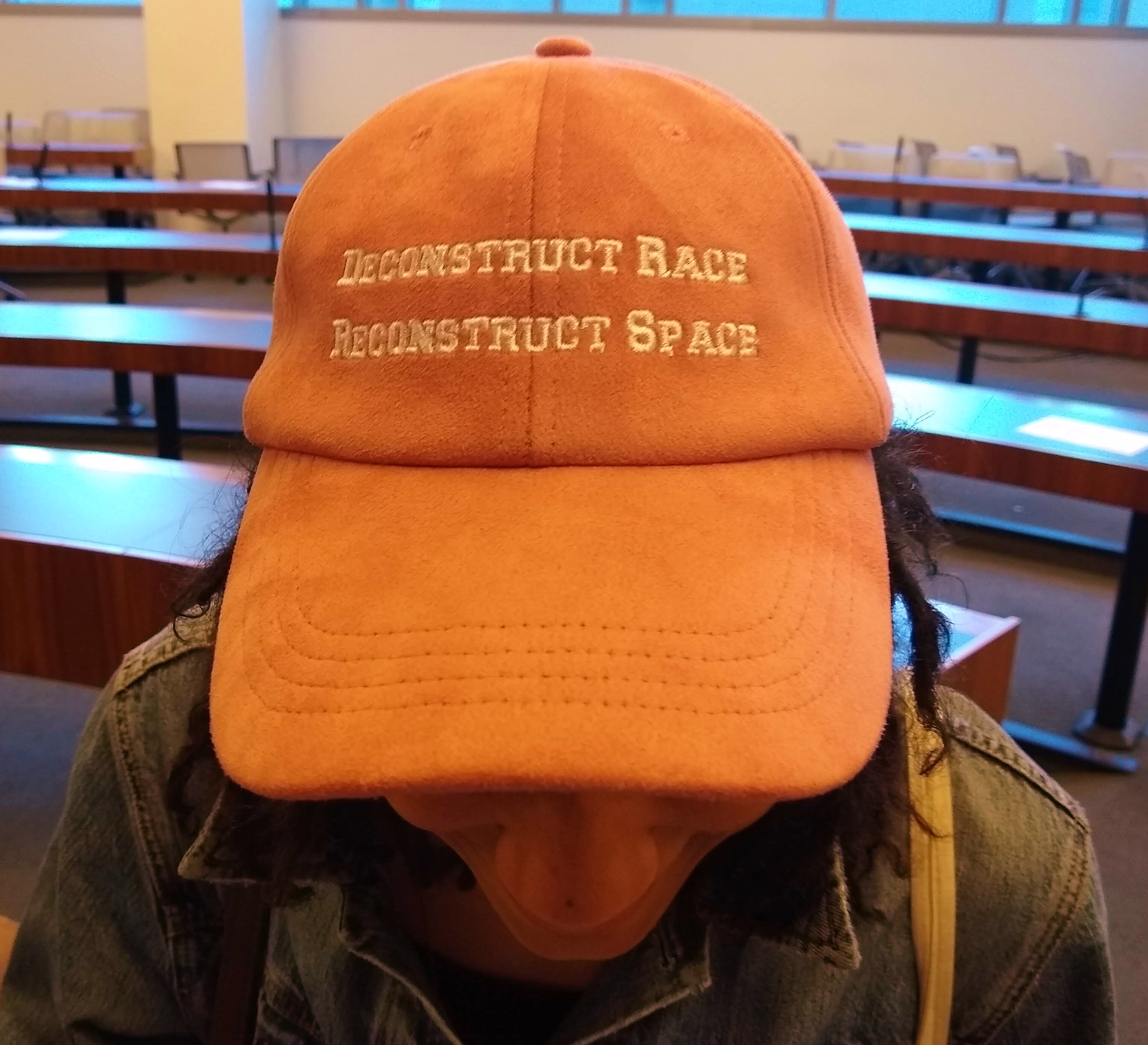 A woman wearing an orange baseball hat that reads, "Deconstruct race.  Reconstruct space."