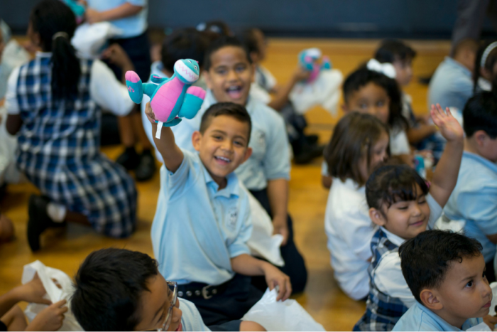 Child holding up stuffed animal toy in crowd of students