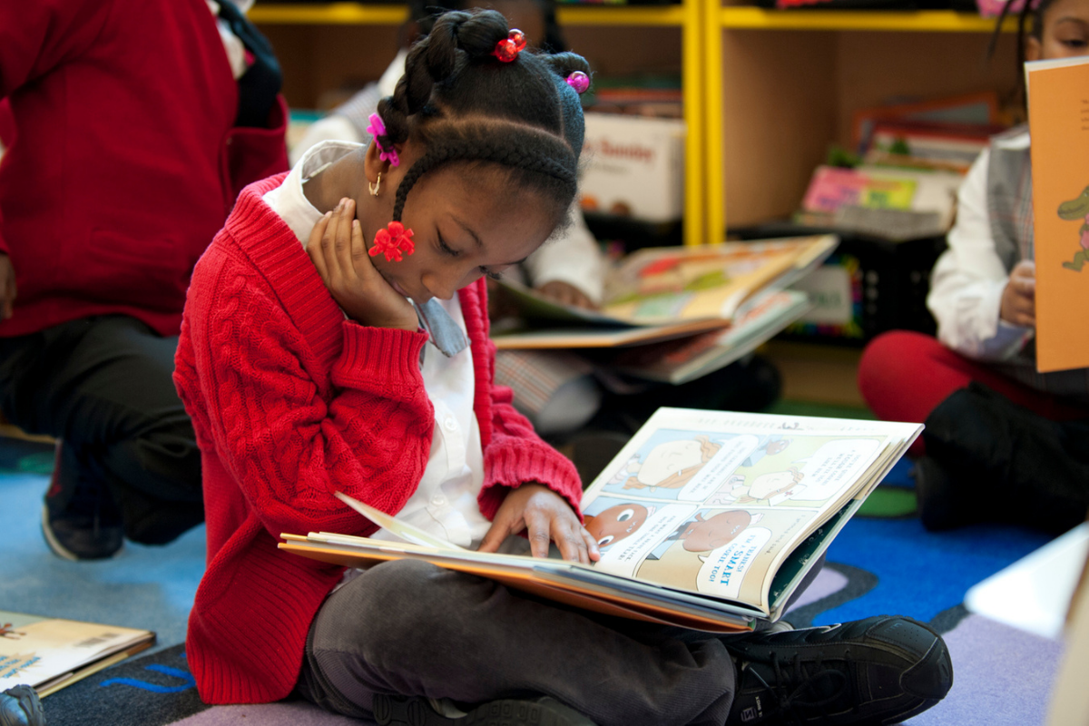 young black student in a red sweater, reading a book in the classroom