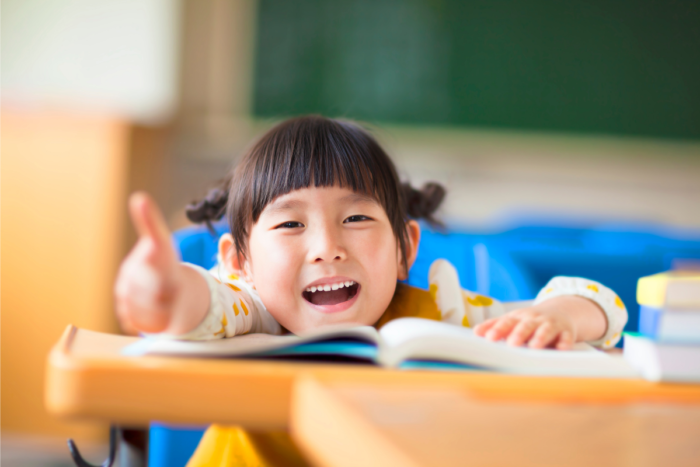 young asian student giving a thumbs up and reading a book