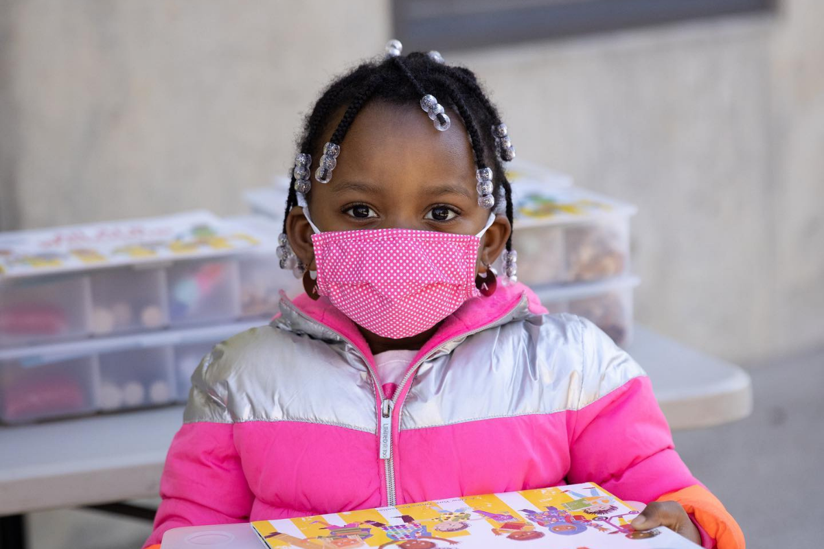 young black girl holding a book, wearing a pink mask