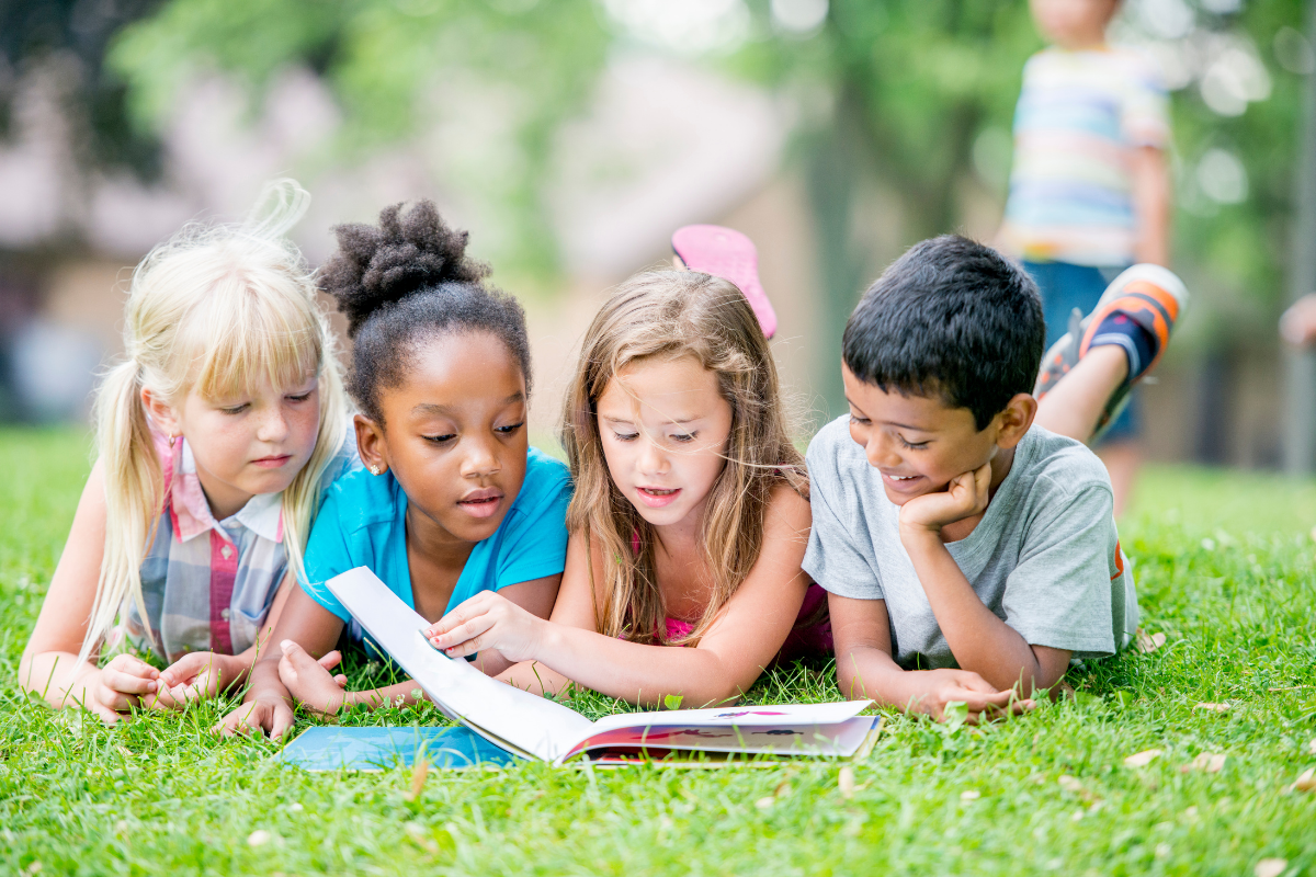 four kids reading books on the grass together