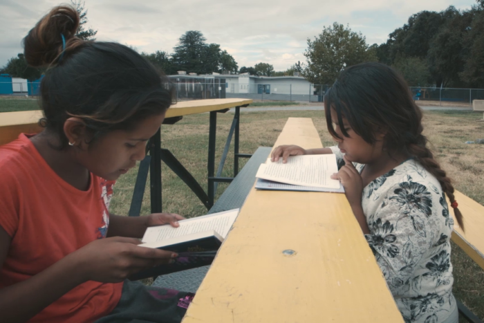 two Hispanic girls sitting on bench reading