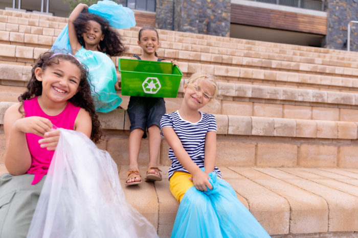 kids sitting on steps with a recycling bin