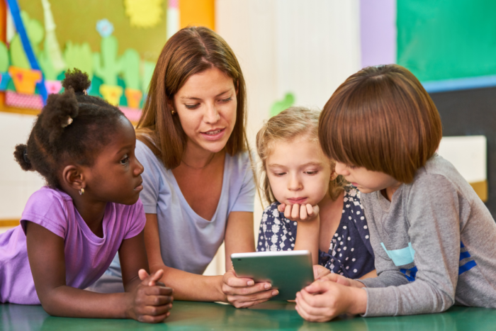 photo of a teacher with three students reading from a tablet