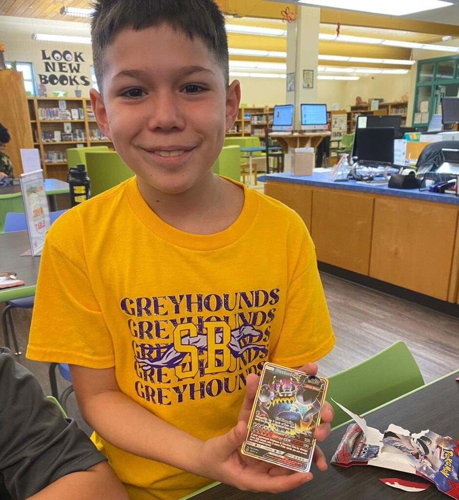 young boy holding a Pokémon card in a school library