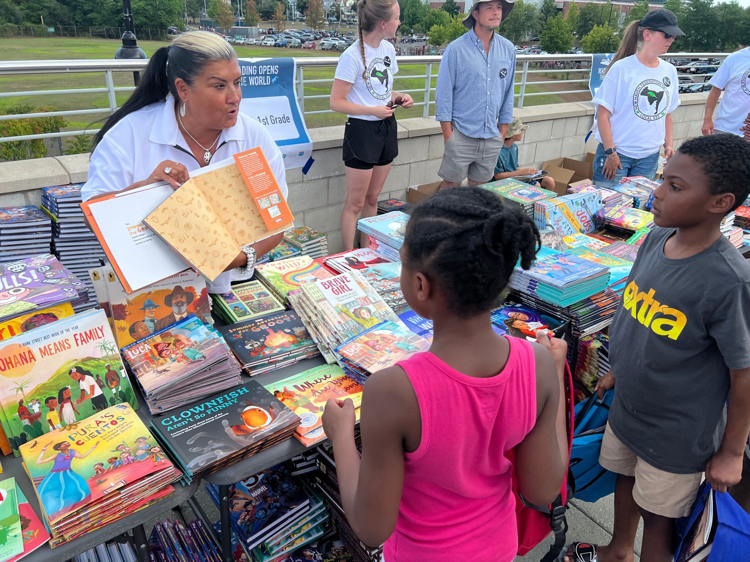 AFT volunteer shows book to two kids at a table full of books.