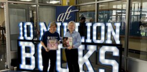 image of Kyle Zimmer, CEO of First Book, and Randi Weingarten, President of the American Federation of Teachers, posing for a photo, both holding children's books. Behind them is a big sign that says, 'AFT 10 Million Books'.