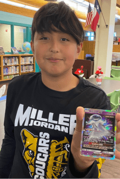 boy holding up a Pokémon card in a school library