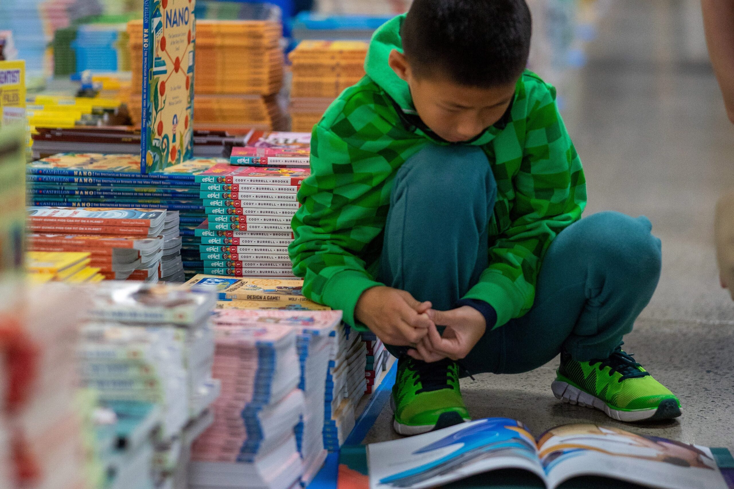 young boy crouching down, reading a book.