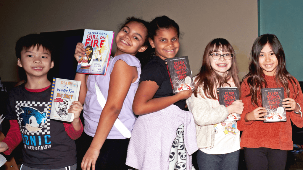 a group of kids, smiling and holding up books. 