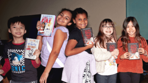 a group of kids, smiling and holding up books.