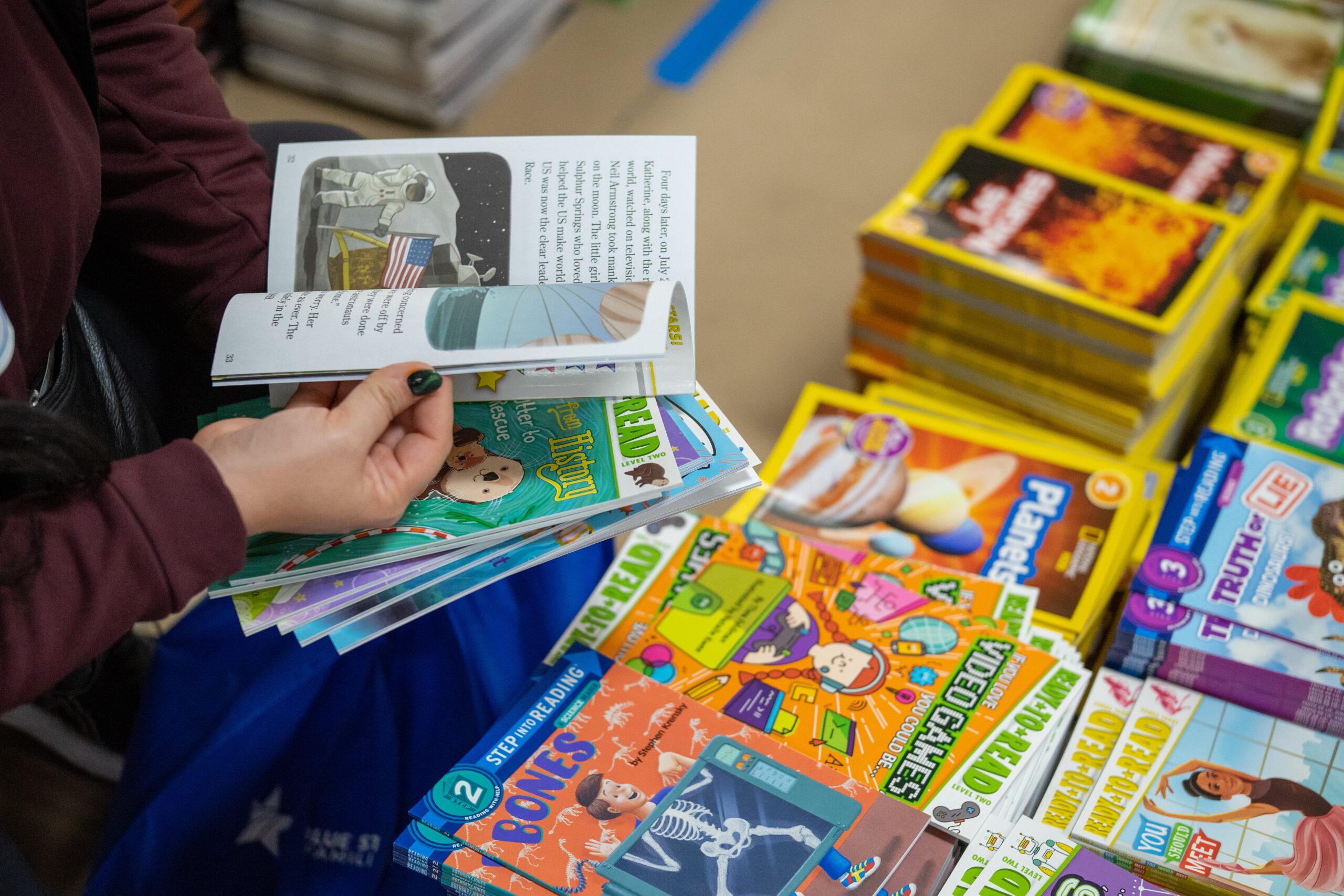 image of a person's hands flipping through a book, amongst stacks of books.