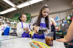 image of two young girls in a classroom, pouring coffee.