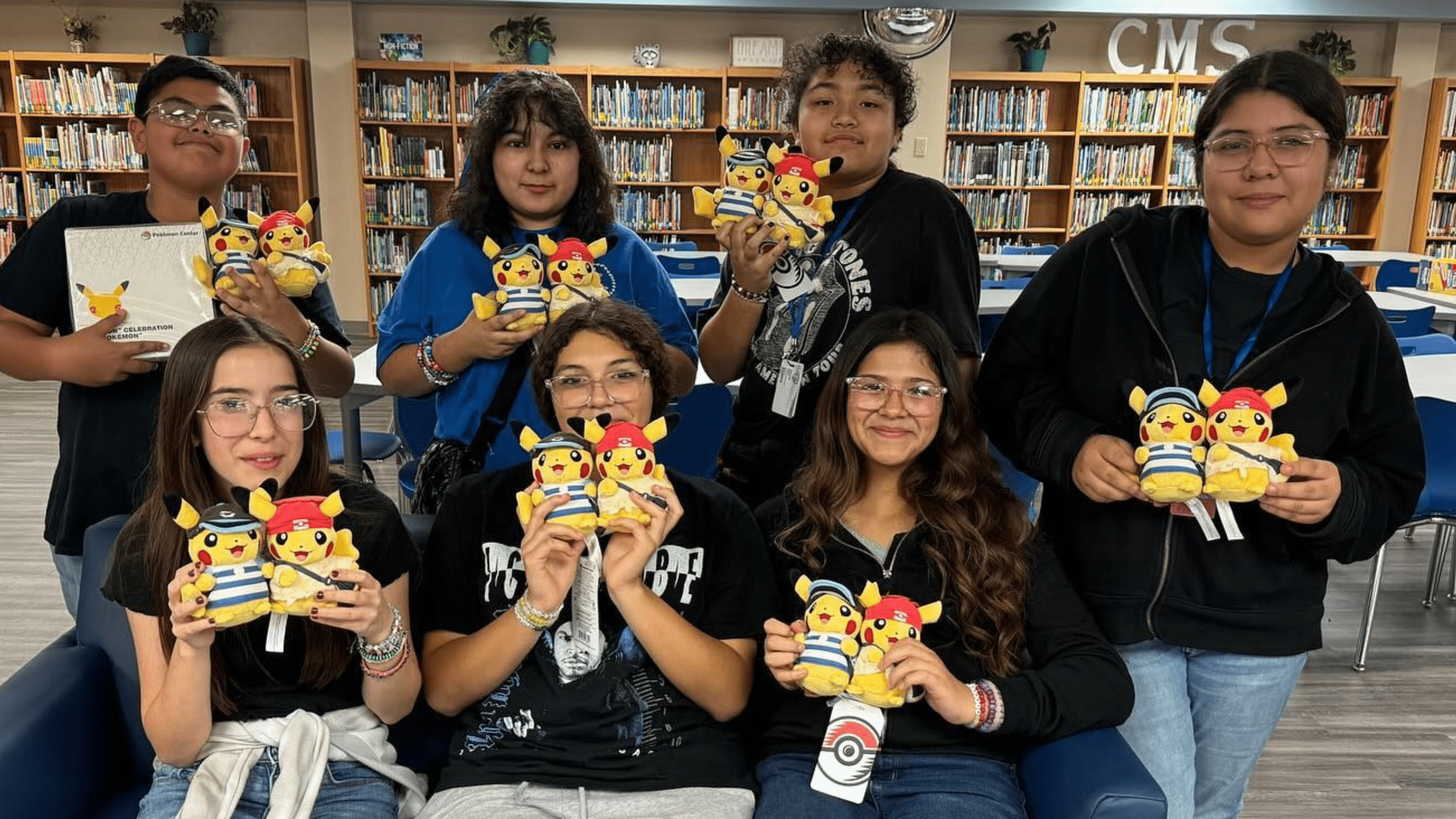 Image of a group of students in a library, holding up Pokémon figurines.
