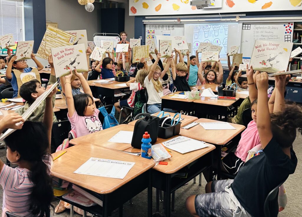 Elementary students holding up copies of a book in a classroom